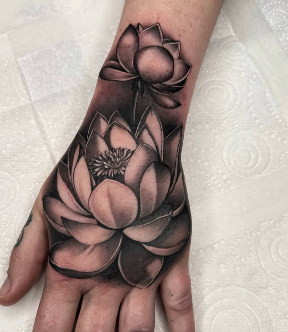 Black and grey lotus flower tattoo with layered petals and smooth gradient shading on the back of the hand