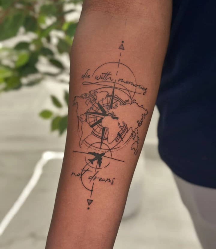 Fine line travel compass tattoo with globe and hand-lettered 'die with memories, not dreams' script on forearm
