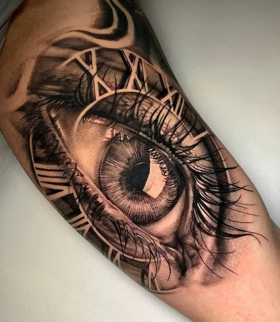 Hyperrealist tattoo of a human eye with Roman numeral clock face detail, layered gray-wash shading on inner bicep